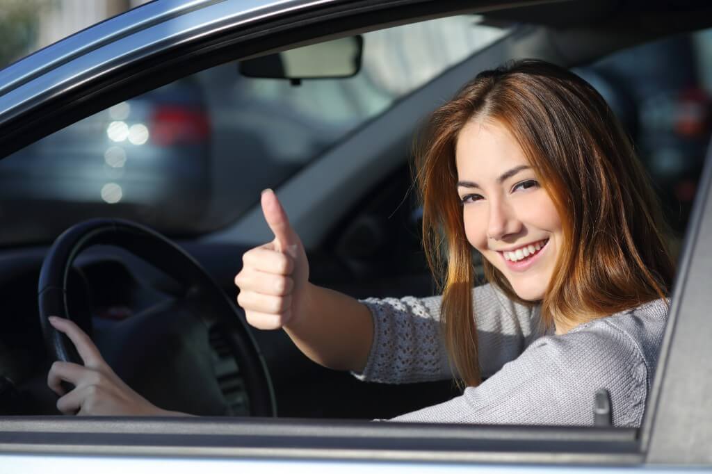 Happy woman inside a car driving in the street and gesturing thumb up